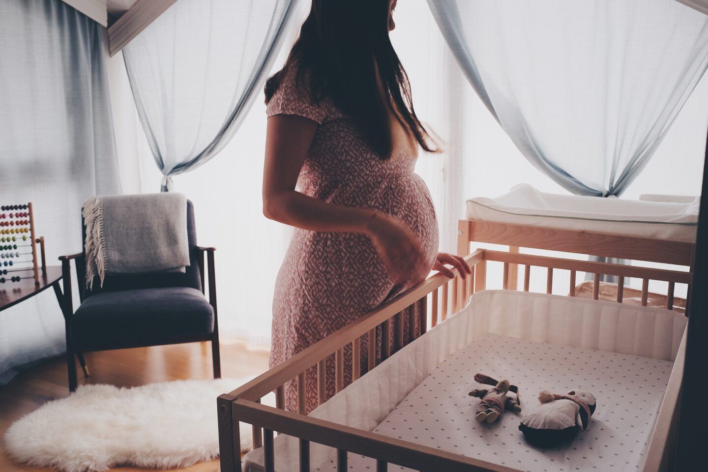 Pregnant person standing above a crib, waiting for baby