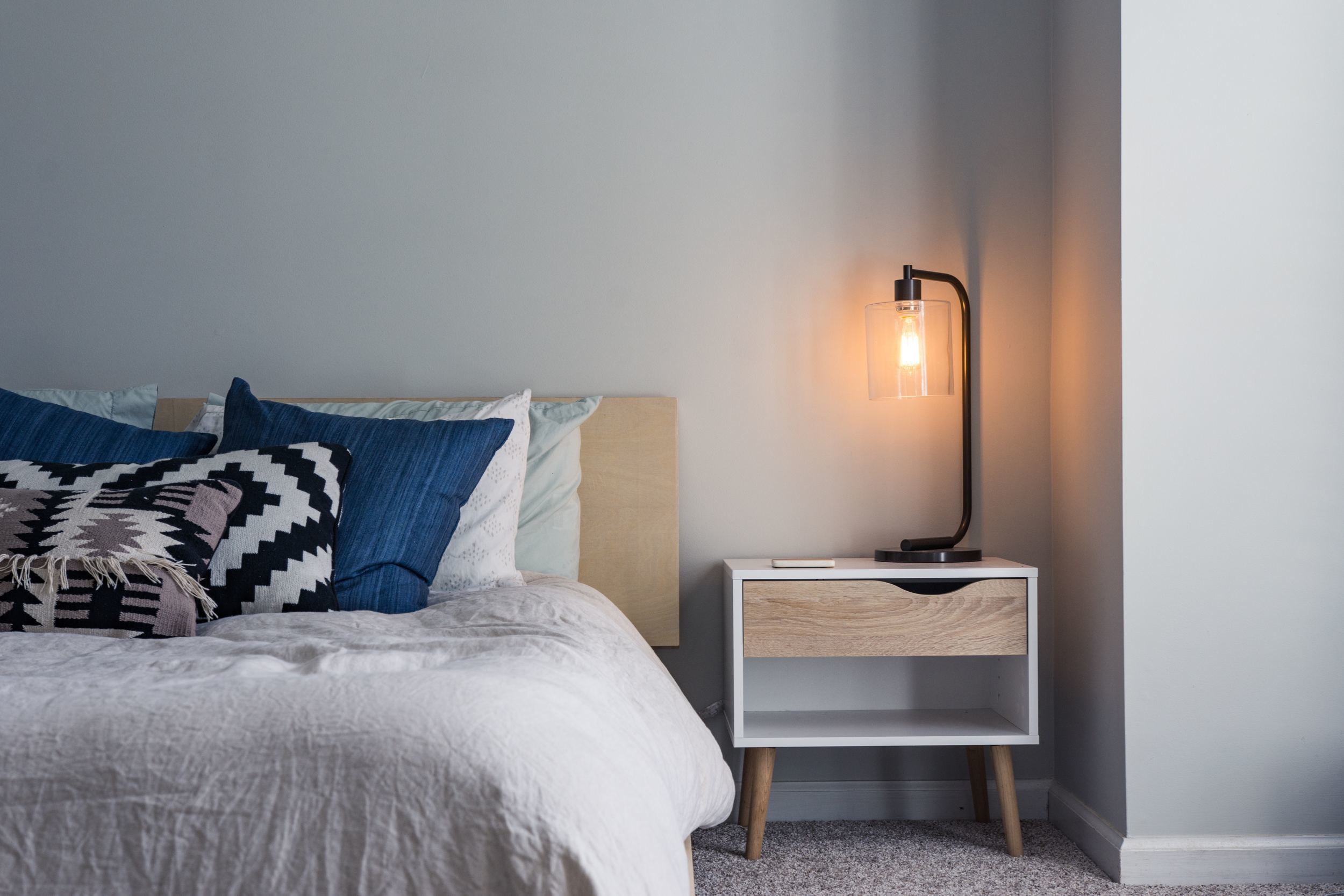 a made bed with a nightstand and an industrial lamp thats turned on