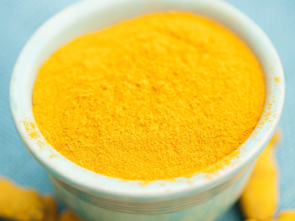 A close up shot of tumeric in a white ceramic dish against a light blue background