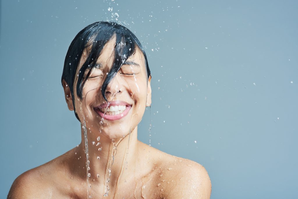 a man sitting under running water smiling against a light blue background