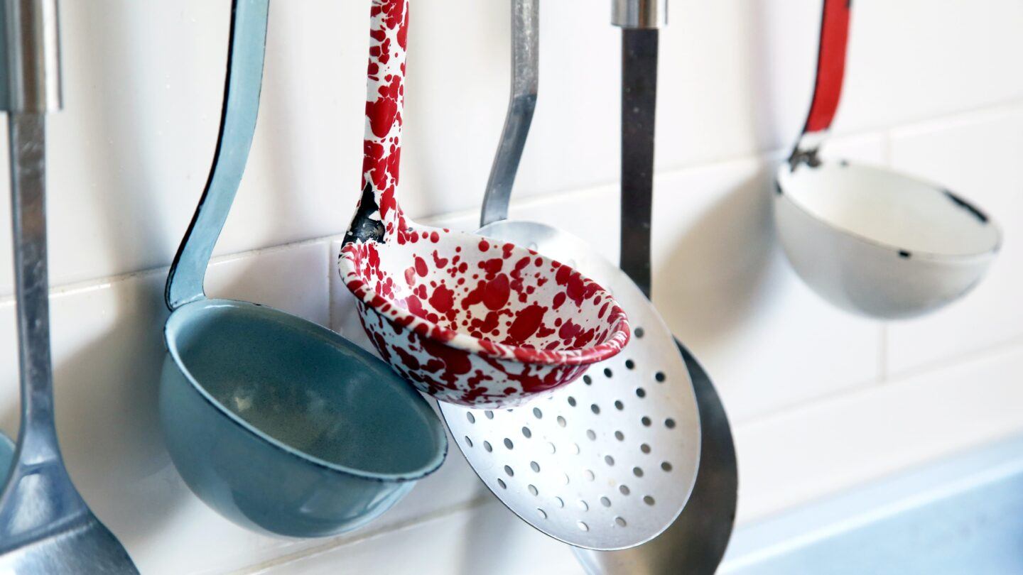 A wall mount holding several different ladles and cooking spoons in a variety of colors, from blue to red