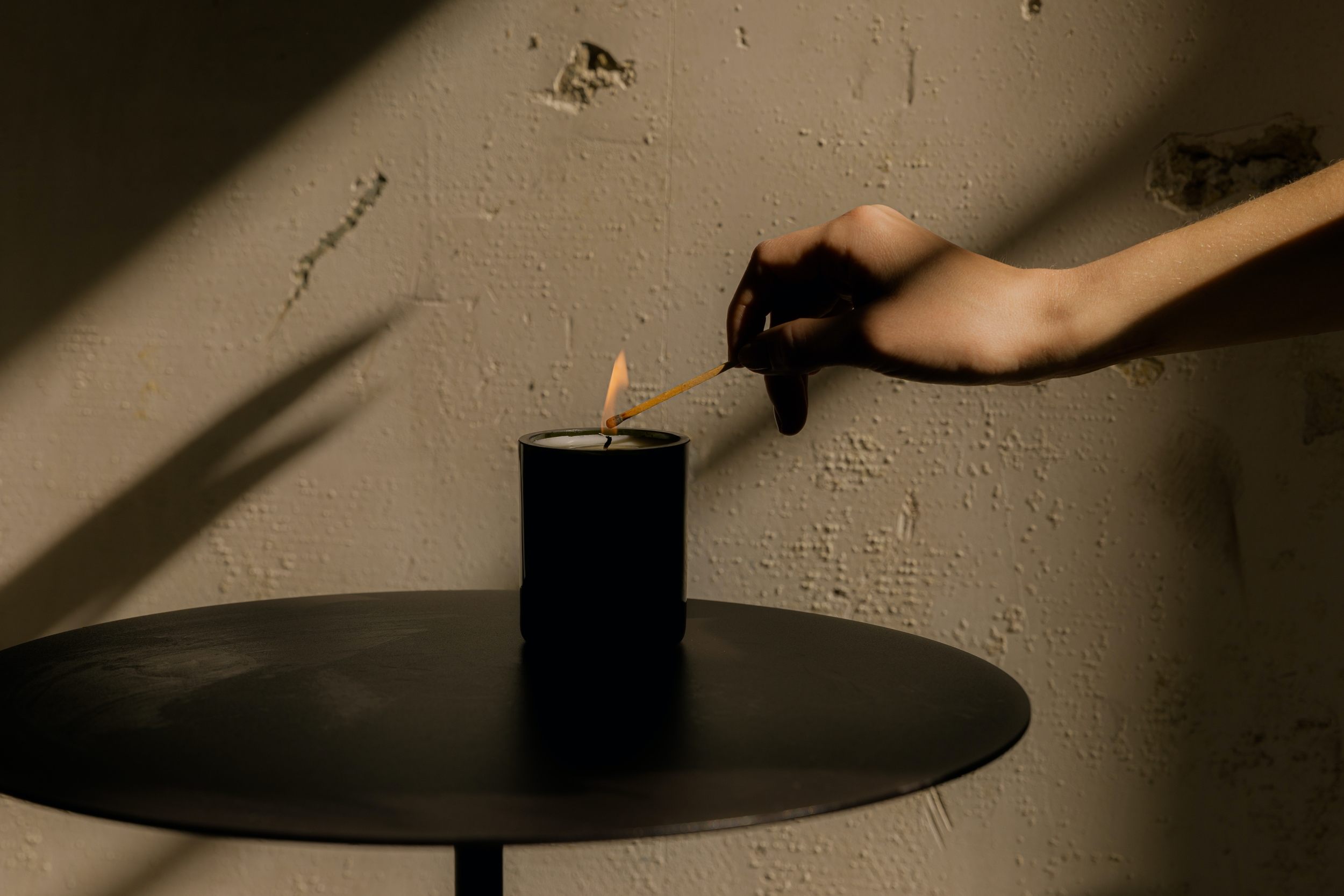 A peaceful side table with a candle on it and someone's leaning over with a lit match, ready to set the tone for a relaxing moment