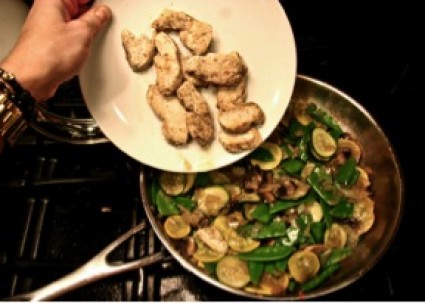 cooked sliced chicken being added to a pan of vegetables