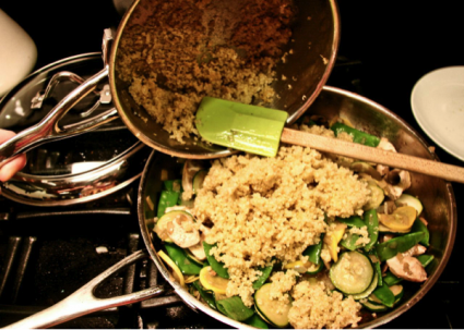 cooked quinoa being added to chicken and veggies in a pan