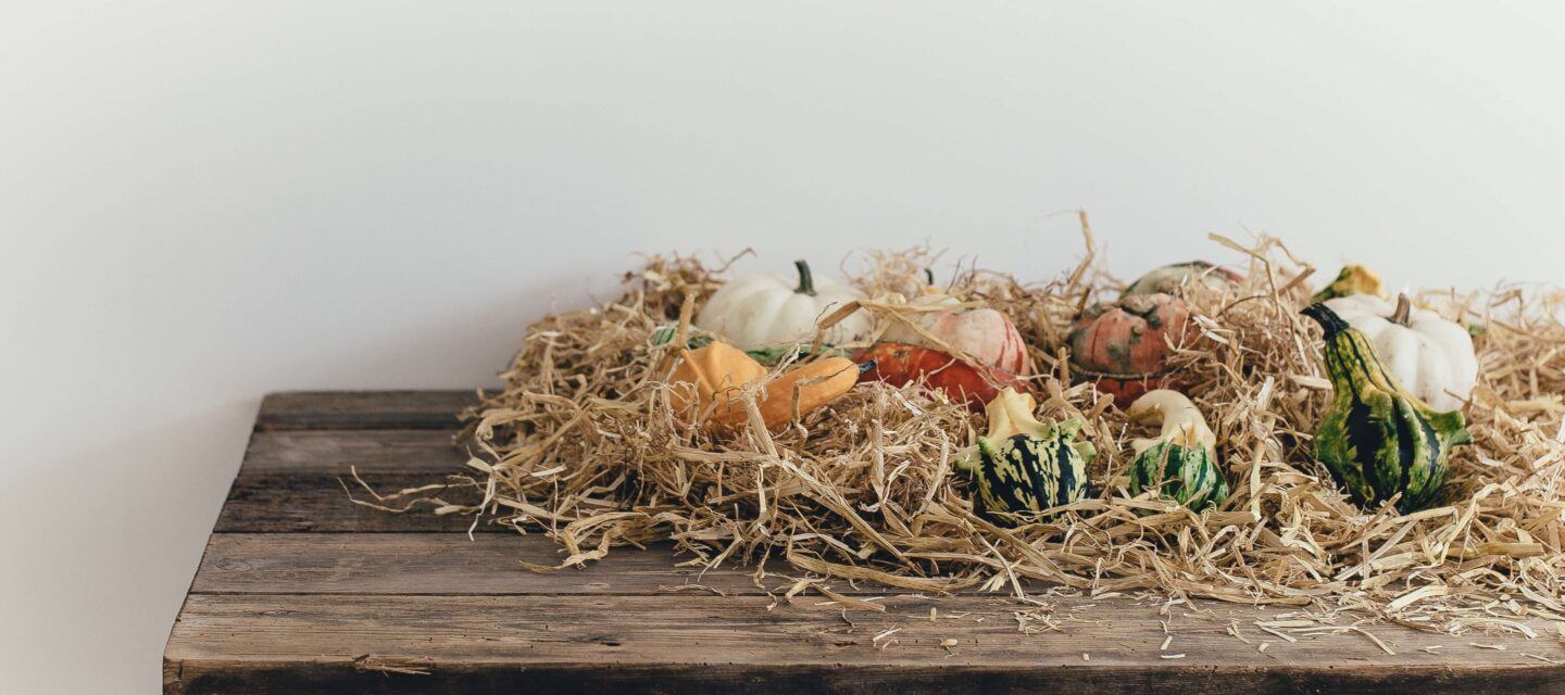 A decorative side table with hay and gourds artfully on It