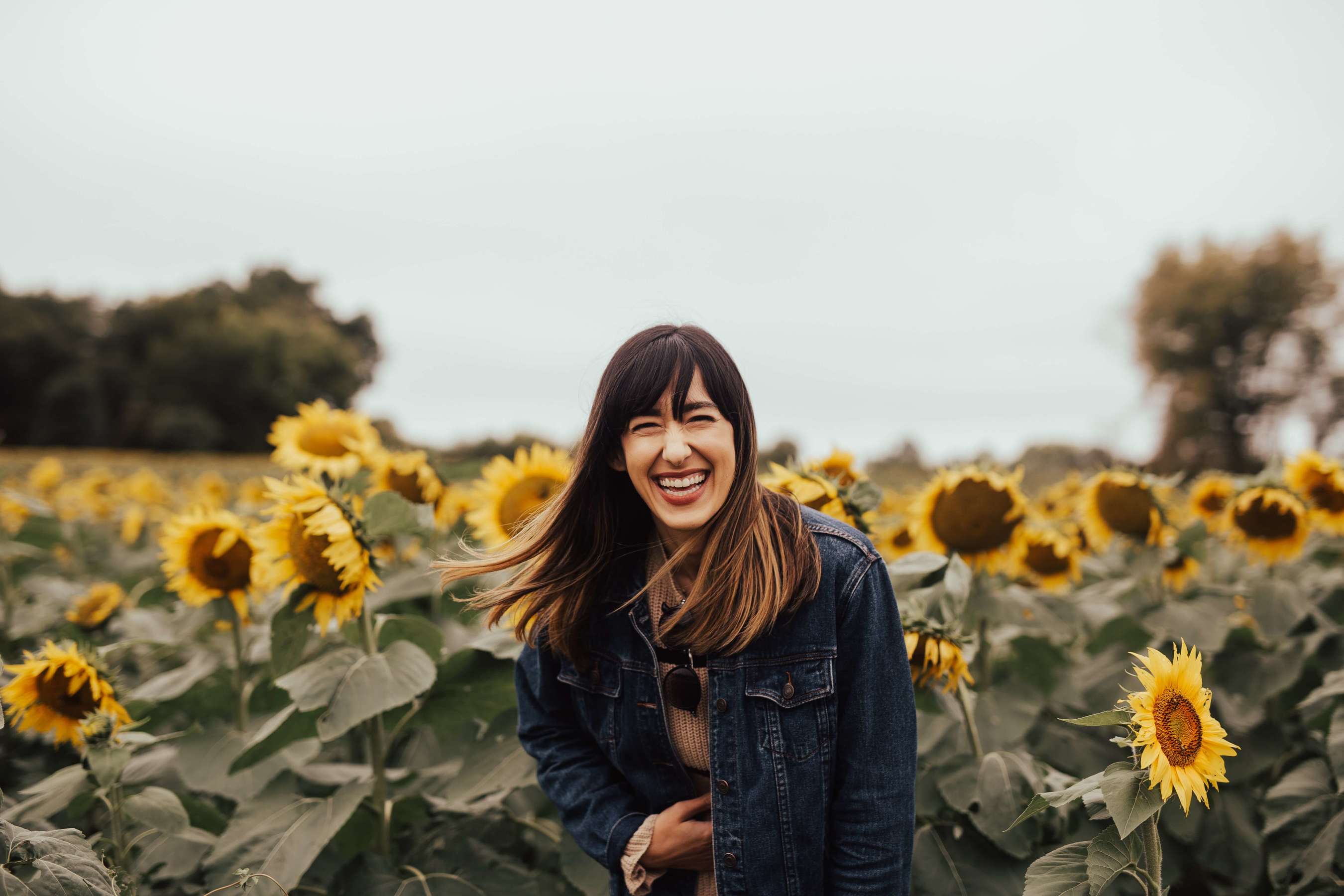 A person standing in the middle of a large sunflower field, holding their belly as they laugh deeply