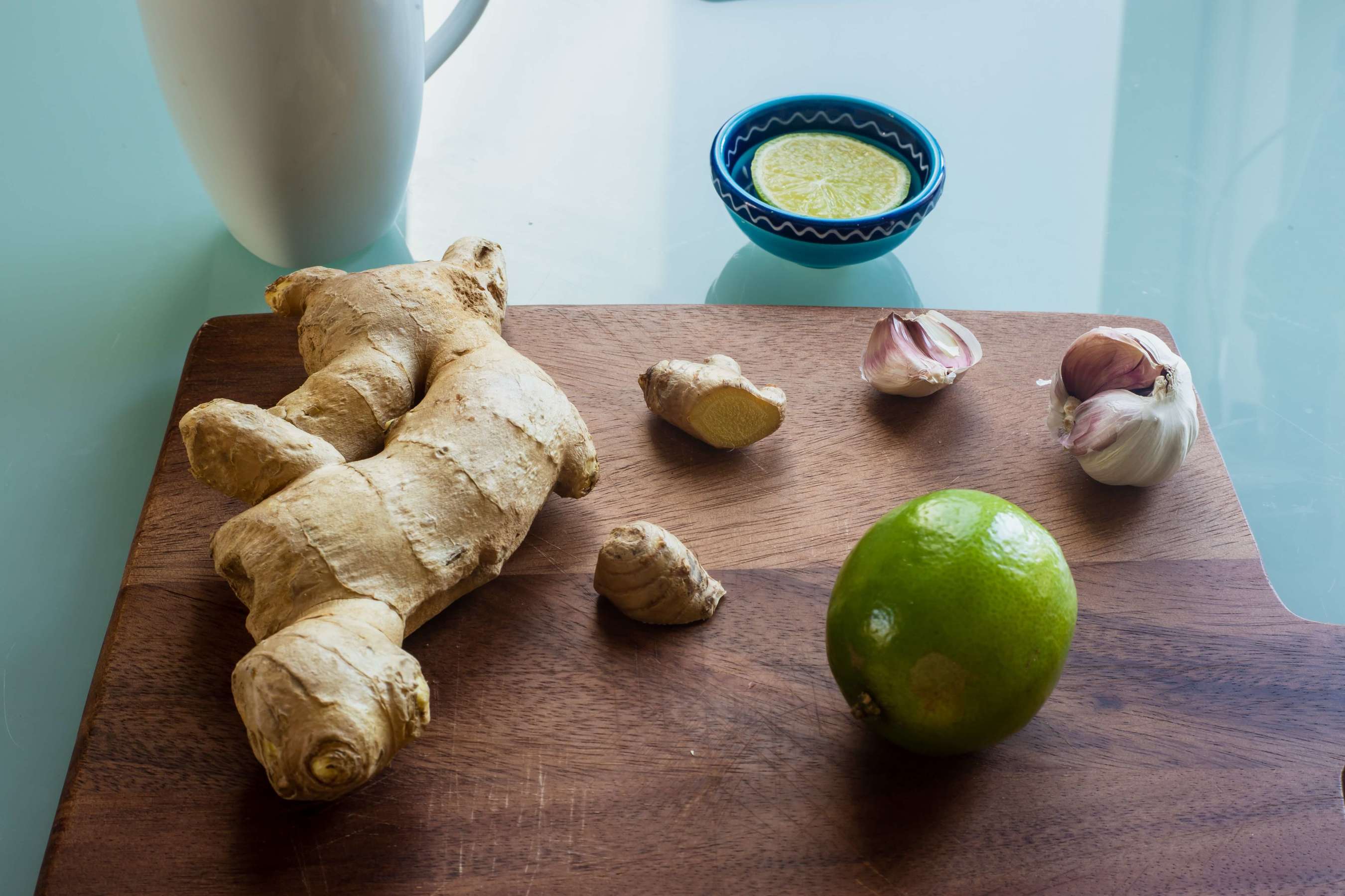 A dark brown wood cutting board with some ginger, garlic, and lime on it - ready to be diced and eaten!