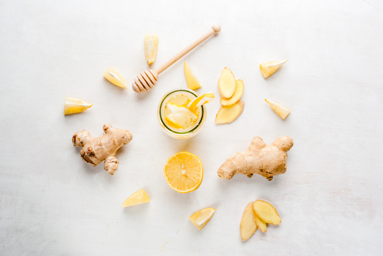 Ginger-lemon drink in a bottle with a straw. Selection of the ingredients of ginger cocktail or tea: ginger root, lemon, honey. On white table. 