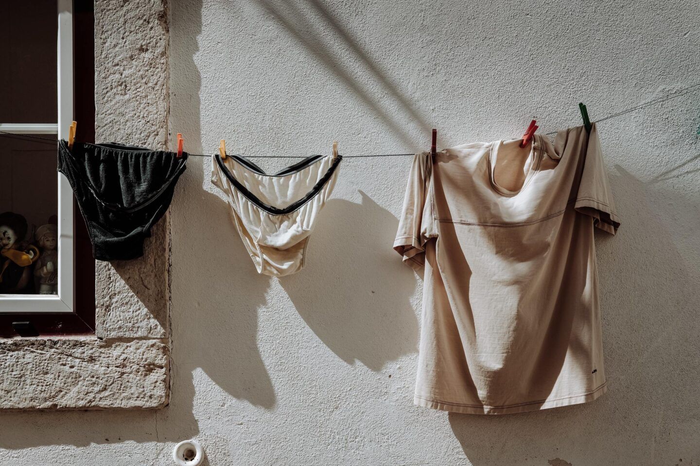 A clothes line out side of a building, and on it hands one beige t-shirt and two pairs of underwear, one black and one white