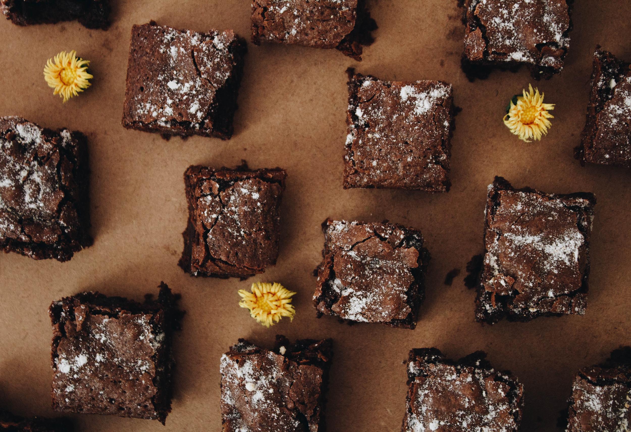 Moist and gooey chocolate brownie bites, on a cutting board with decorative, edible flowers around them