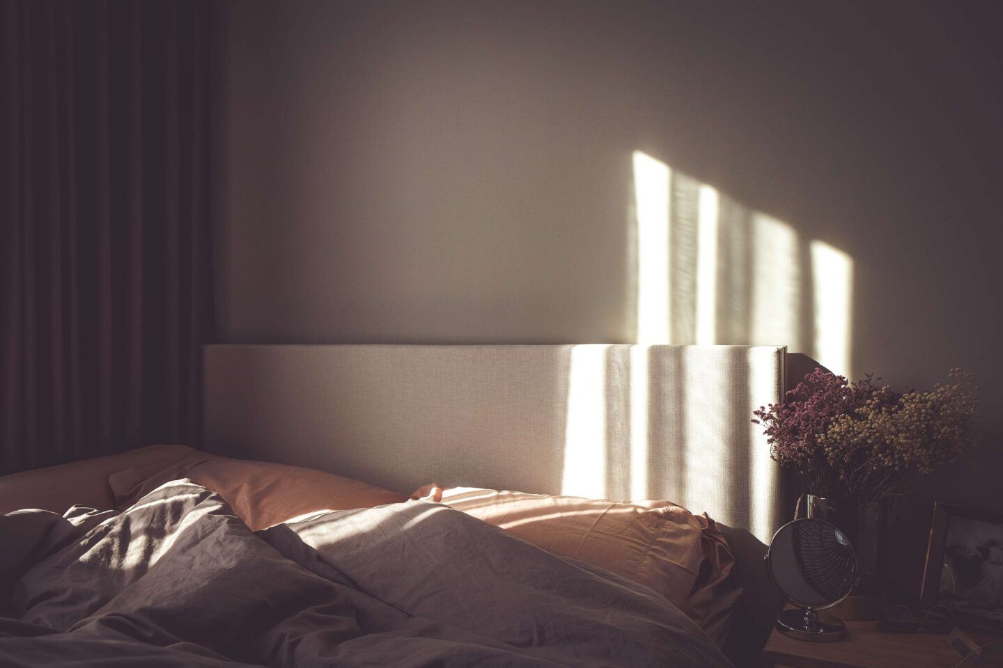 A cozy bed, the sun quietly setting against the bedroom wall