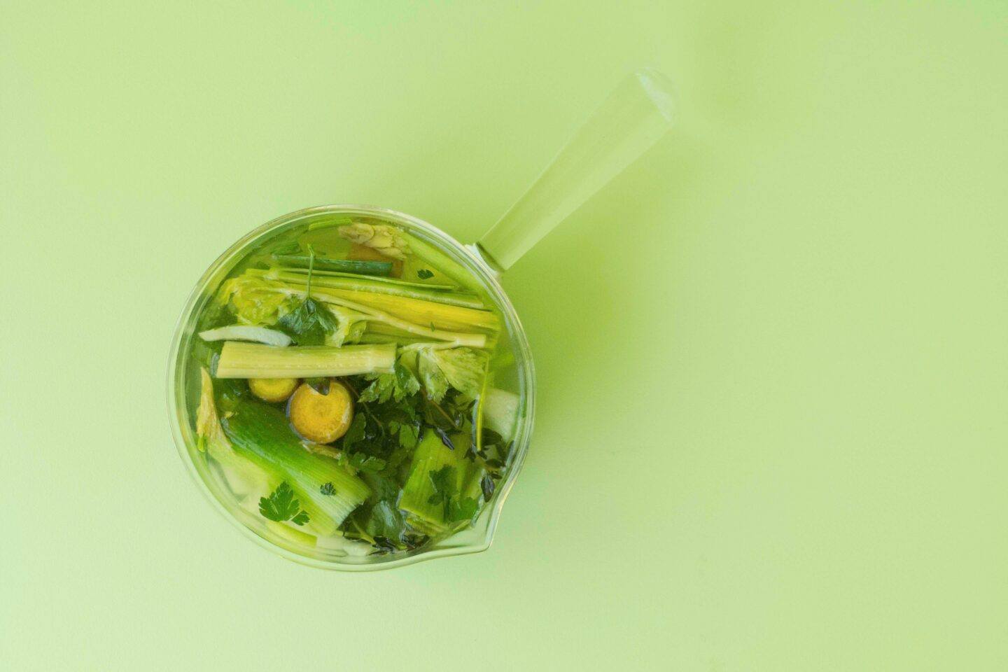 Freshly made broth with some cut veggies, on a vibrant green background