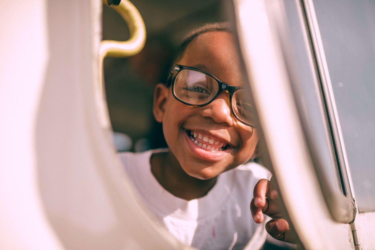 A cute kid with glasses is smiling as they get out of a car