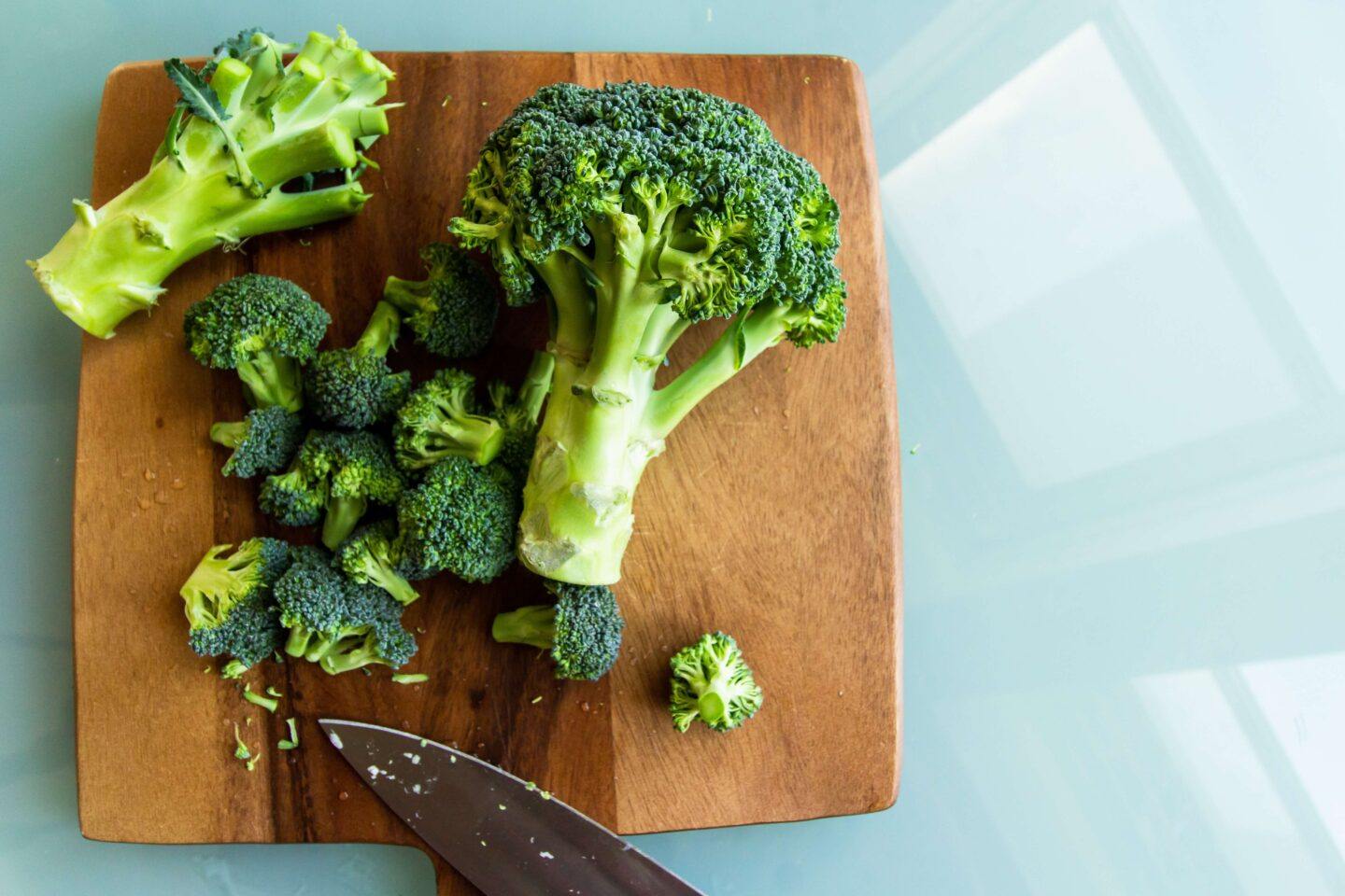 Fresh broccoli, resting on a dark wooden cutting board, ready to be chopped and used in nourishing recipes