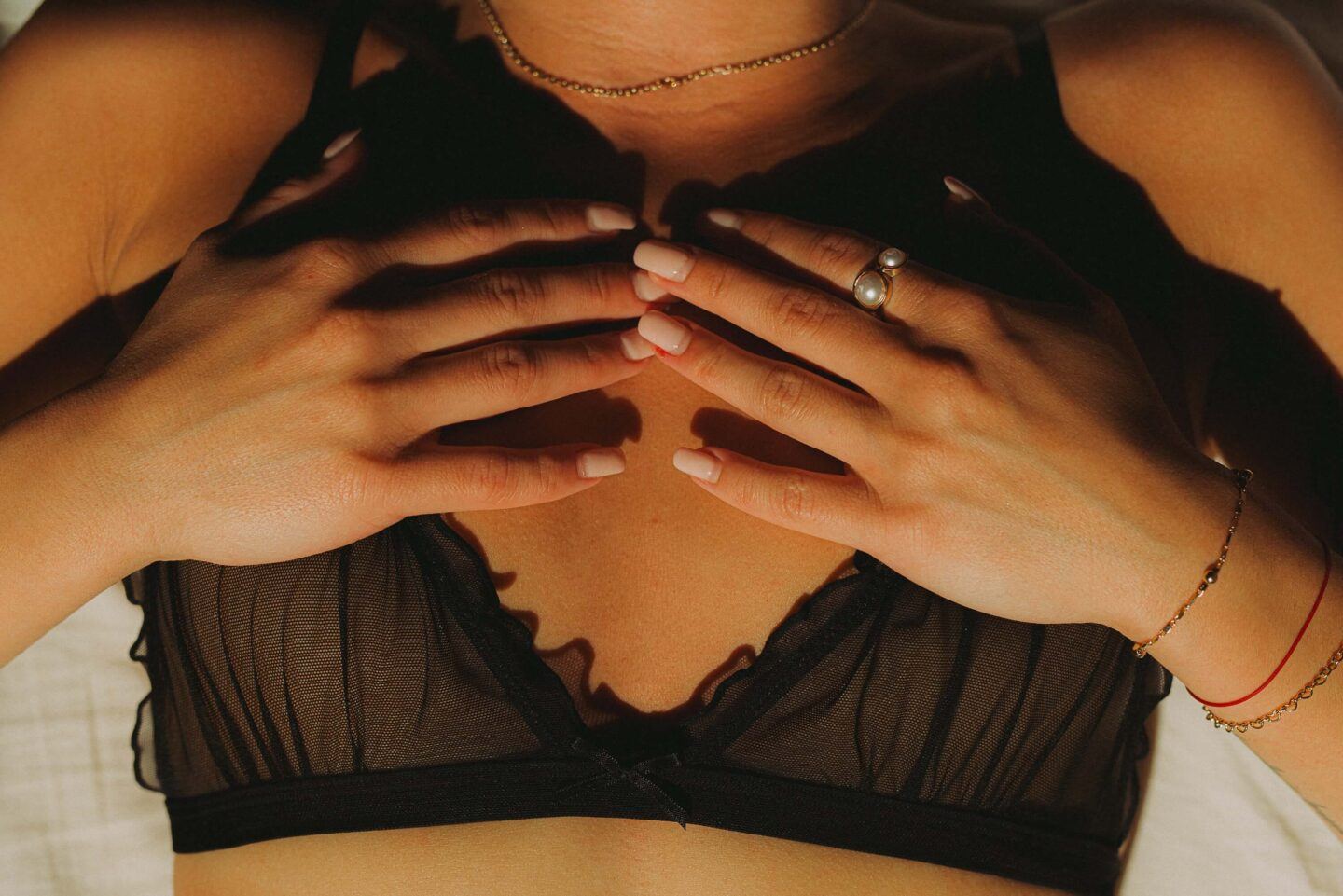 A person is laying down, they have a lace black bra on, and their hands gently are resting on their chest