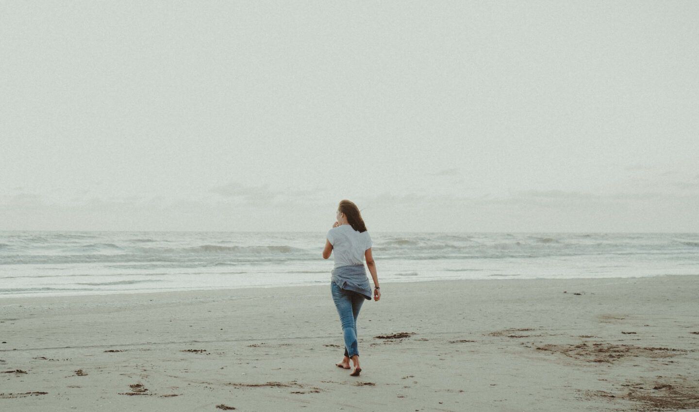 Someone peacefully walking on a sandy beach, barefoot.
