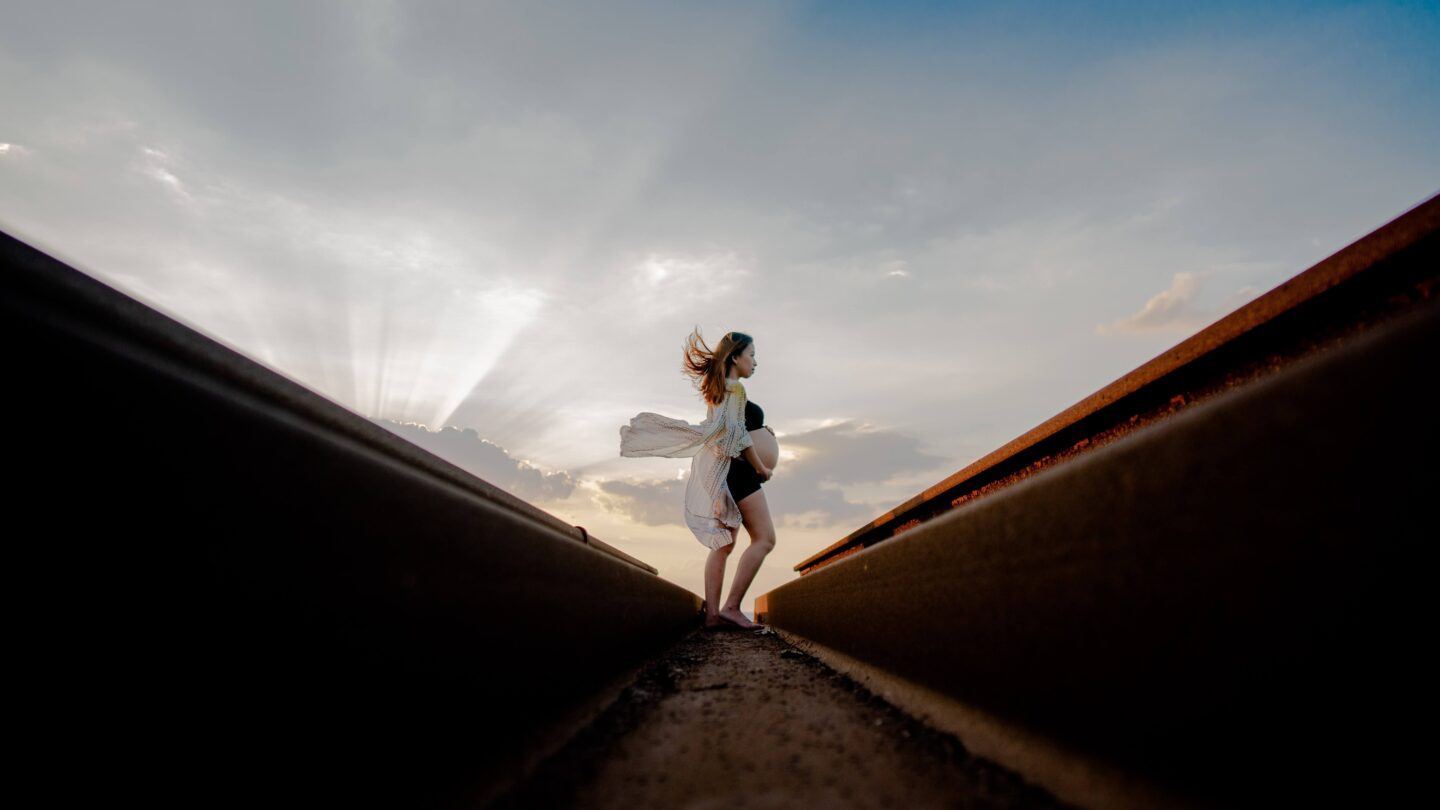 Someone pregnant is standing in the distance, radiant, with a silk shall flowing in the wind behind them