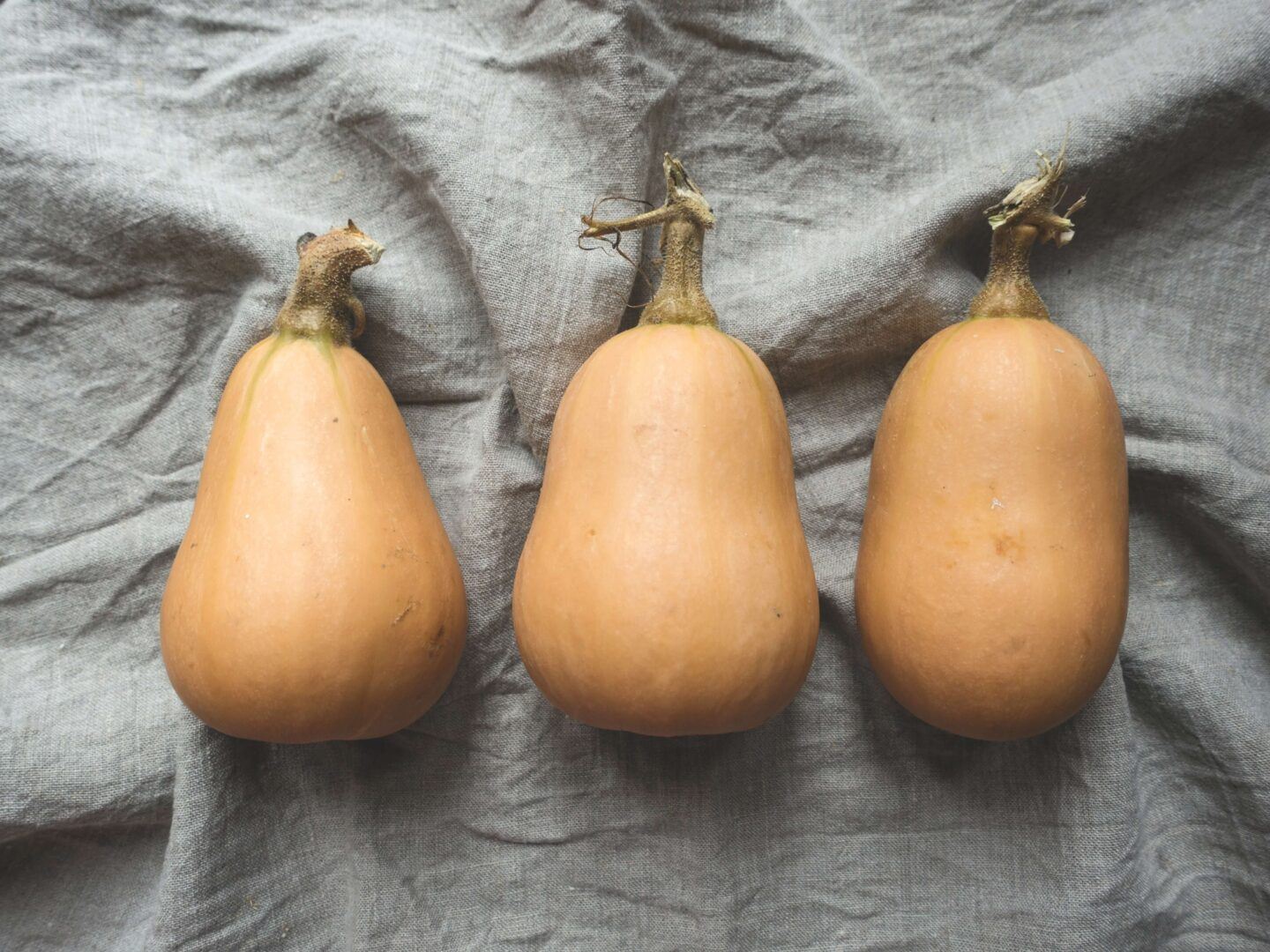 3 pale orange gourds resting on a grey sheet
