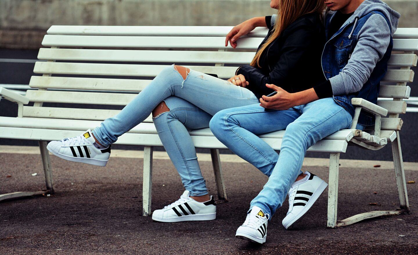 a couple in matching jeans sit on a bench, in each others arms