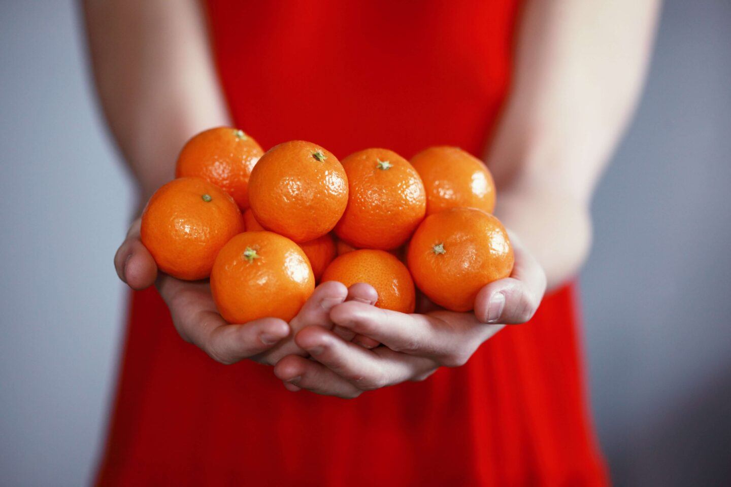 A woman in a vibrant red dress holds oranges, symbolizing good fortune