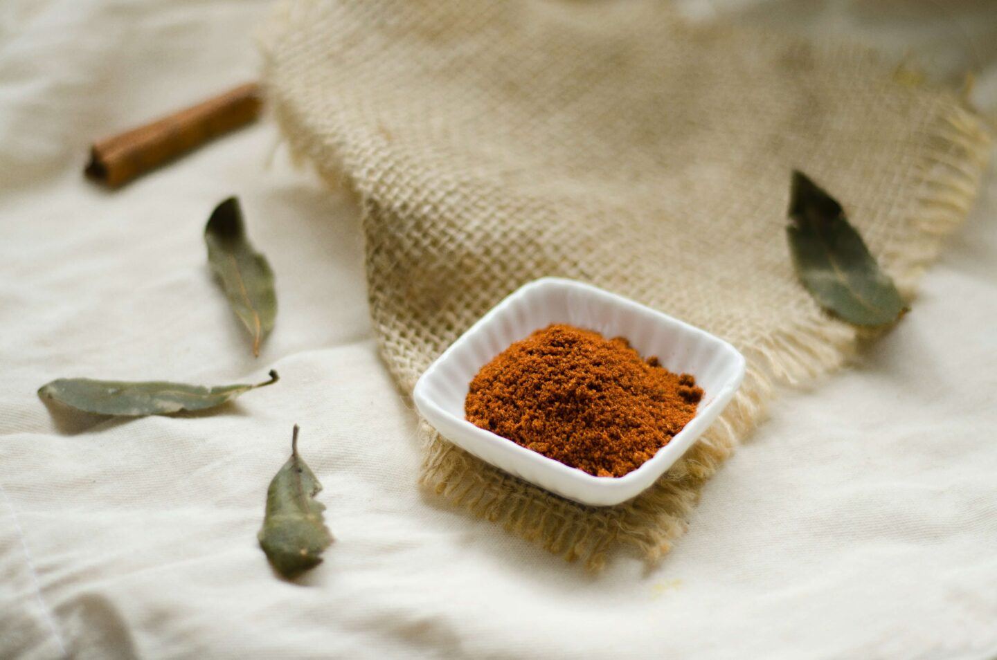 some bright orange turmeric and a few bay leaves rest peacefully on a beige tablecloth