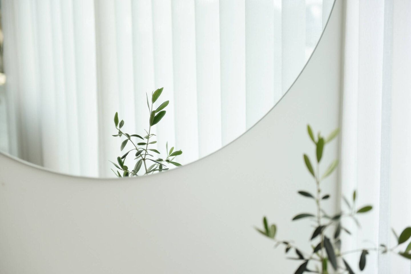 A minimalist white bedroom with a dairy mirror, and in tis reflection: green plants and leaves