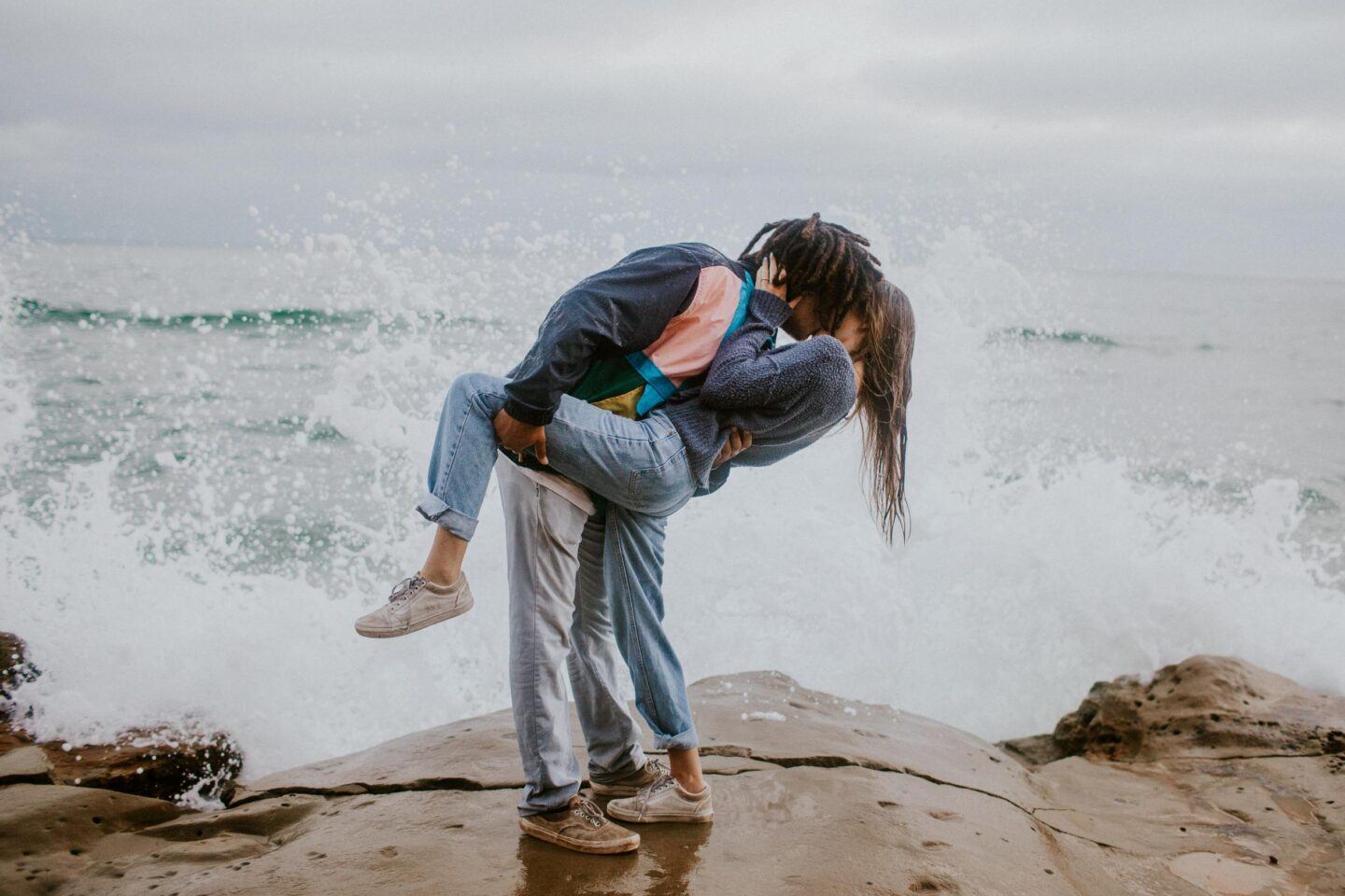 A couple in love kiss passionately on a beach, with waves crashing behind them