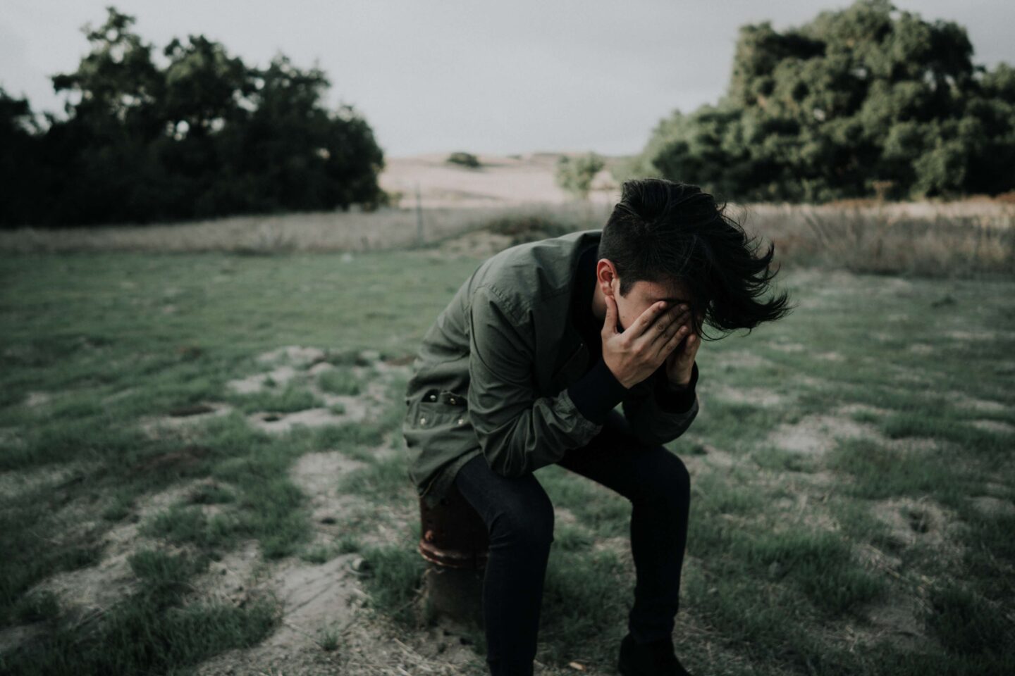 A person in the middle of a field, hunched over in pain clutching their head