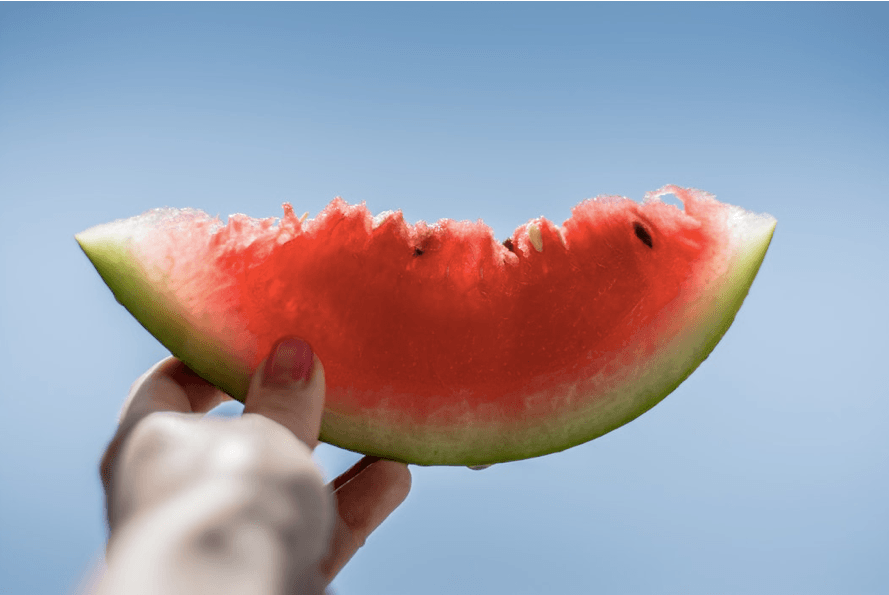 someone holding a slice of watermelon up to a blue sky