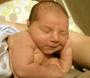 A newborn sleeping in her mom's arms with a slight smile on her face