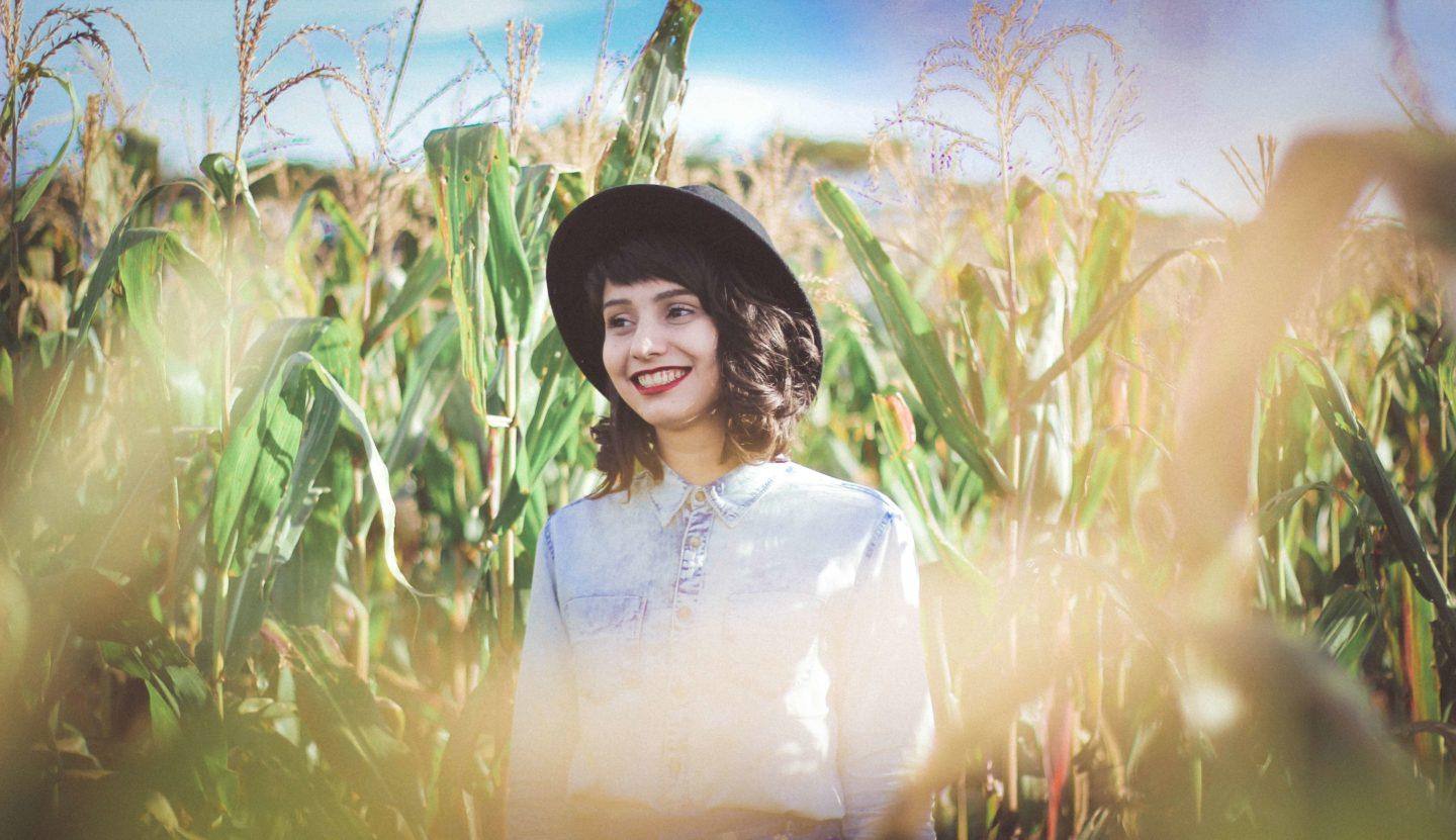 a white woman wearing a black hat standing in a corn field