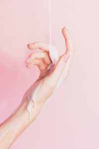 A white woman's hand against a light pink background with pink liquid flowing down her hand