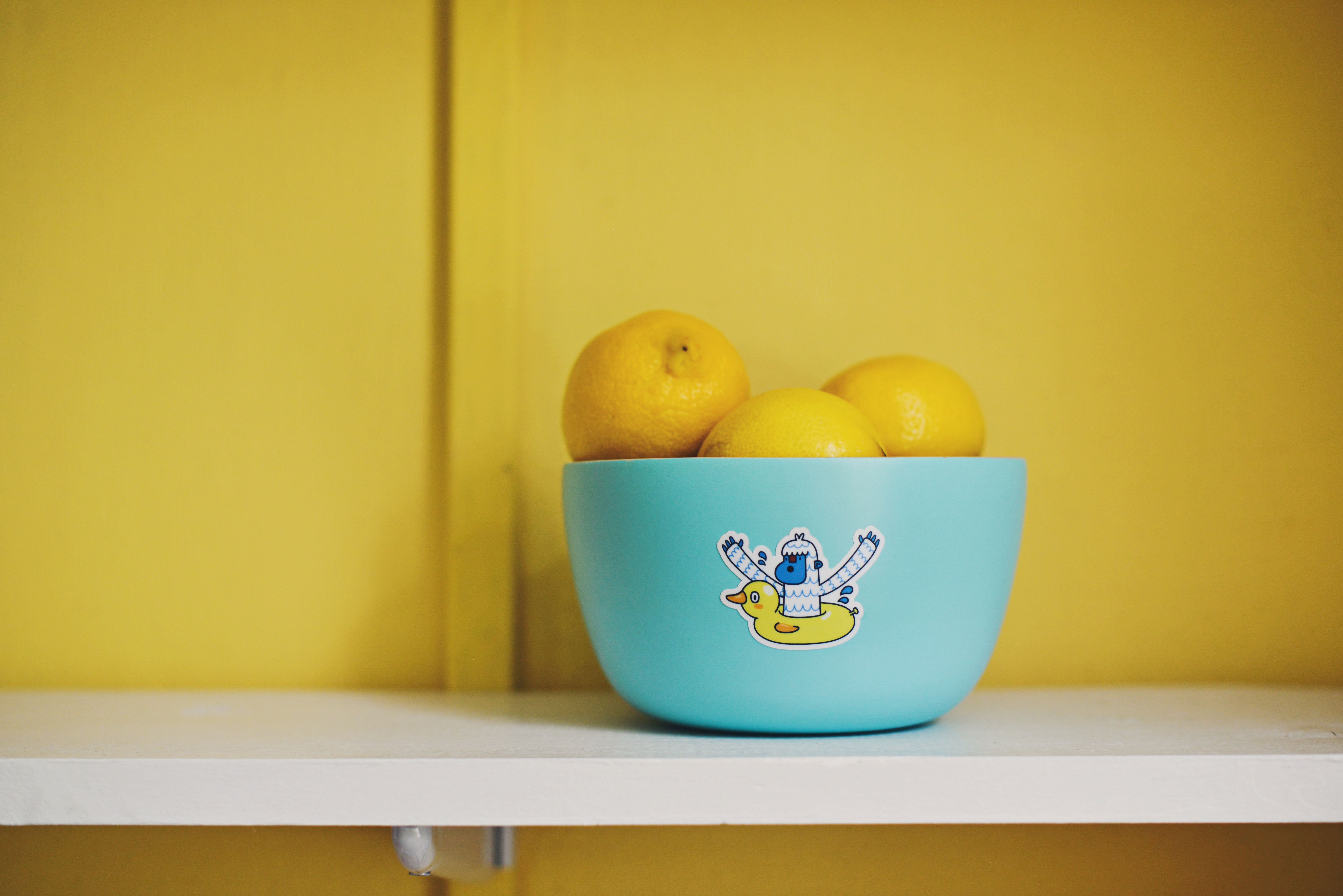 lemons in a blue bowl against a yellow wall