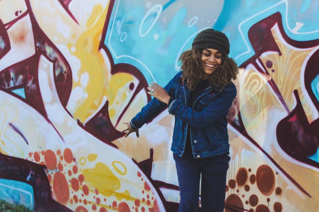 black woman standing happily against an art filled wall