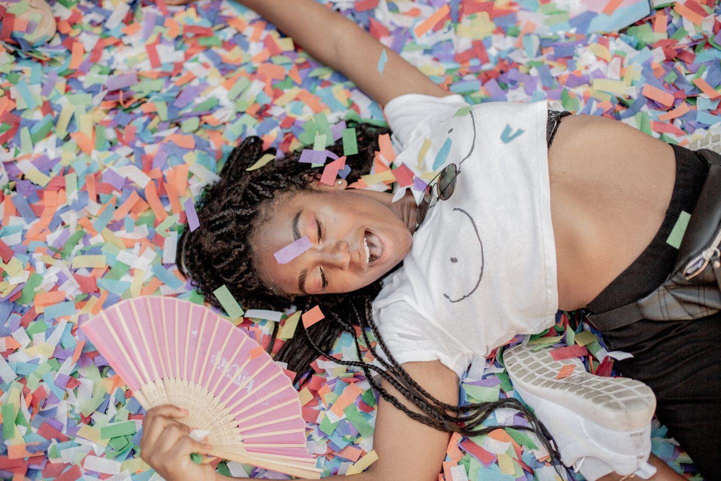 Woman celebrating, lying in colorful confetti