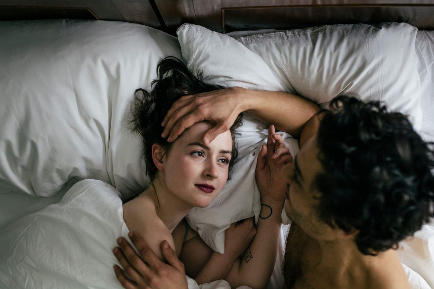 Couple in Hotel bed caressing. The woman is looking into the man's eyes
