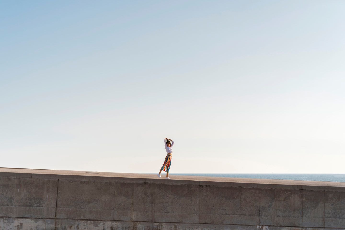 far away shot of a woman standing near beach with blue clear sky
