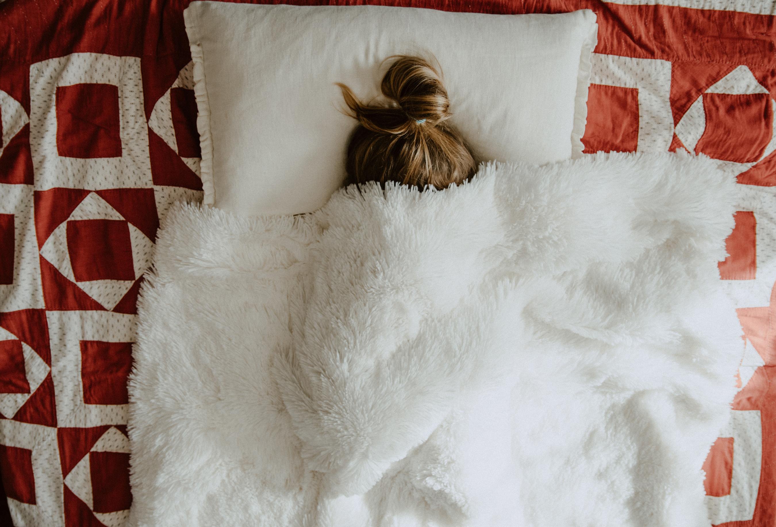 someone laying in bed, with the blankets covering their face. 