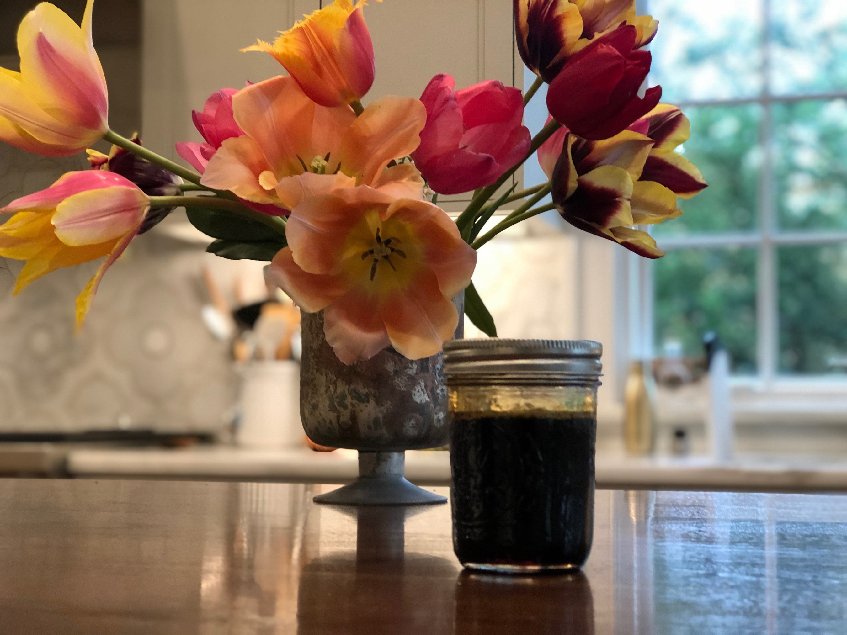 a jar of dandelion butter next to a vase of flowers