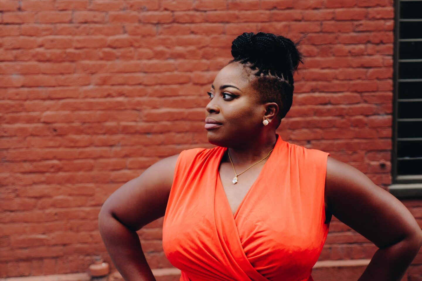 Woman in orange shirt standing by brick wall