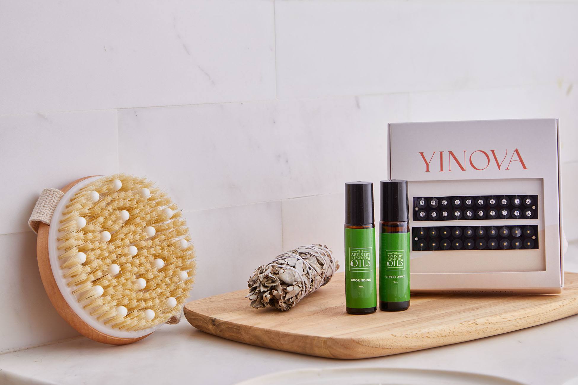 a dry brush, sage, essential oils, and an ear seed kit sitting on a marble bathroom sink