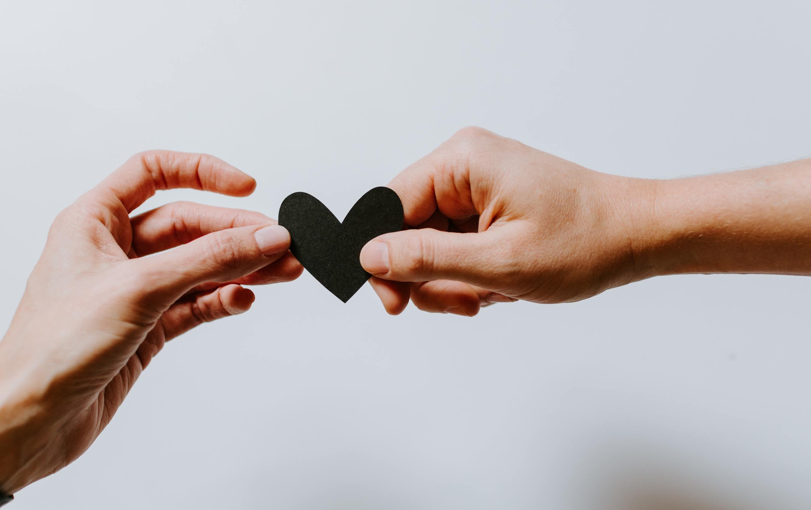 Two hands holding a heart paper together